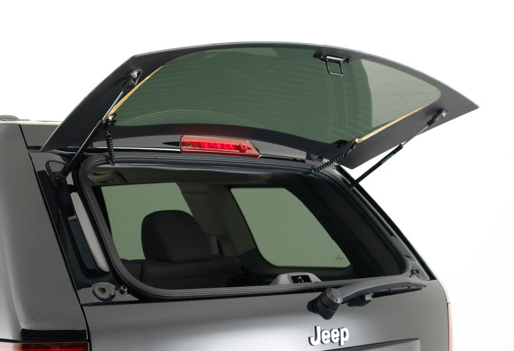 Rear liftgate of a gray Jeep SUV open, showing the cargo area and a raised rear window