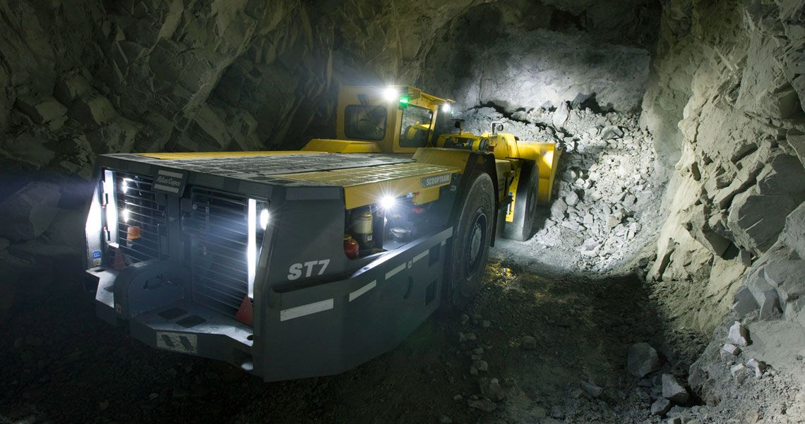 Yellow mining vehicle driving through a rocky tunnel inside an underground mine