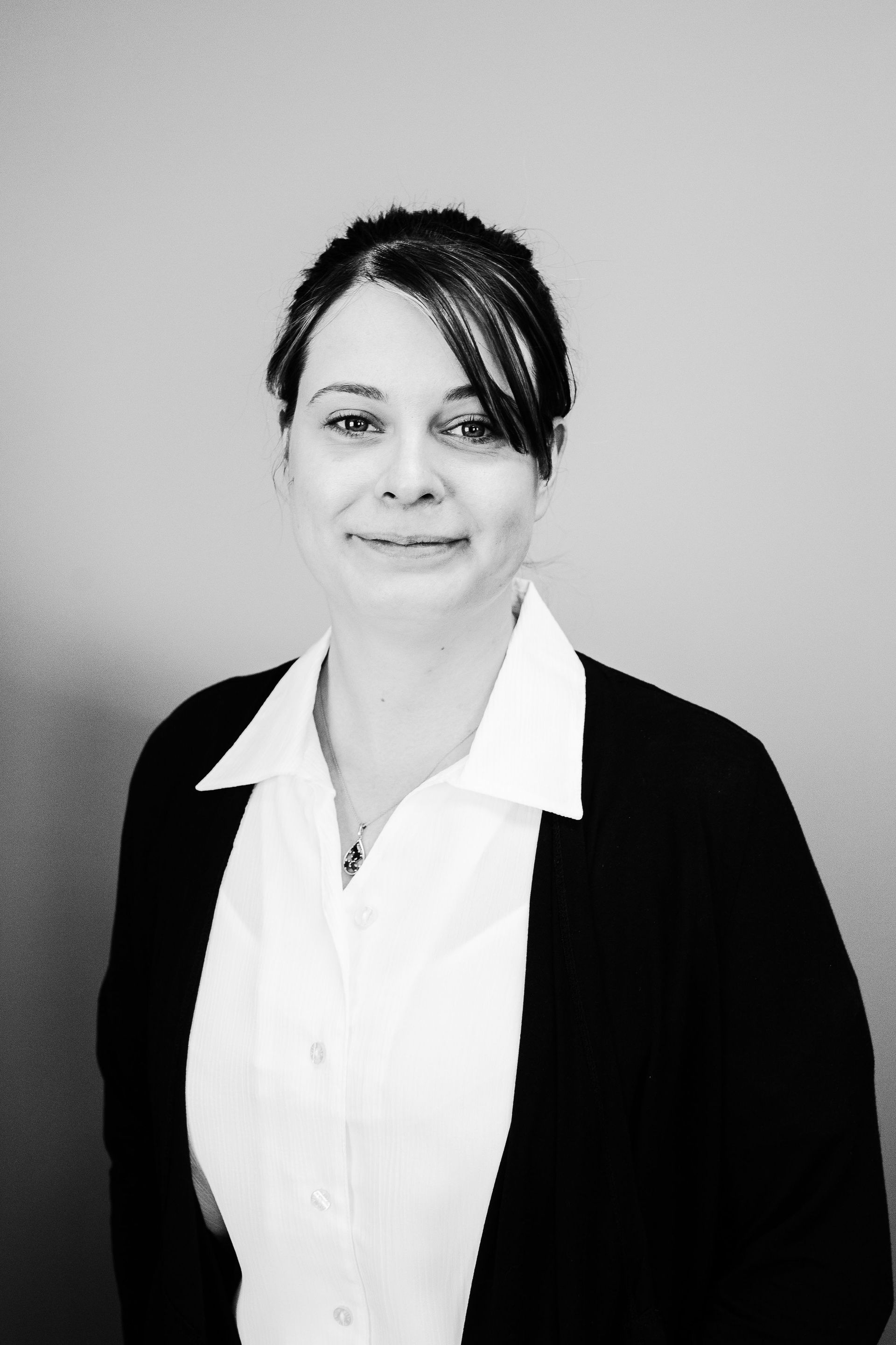 Portrait of a woman in a white shirt and dark blazer against a plain gray background