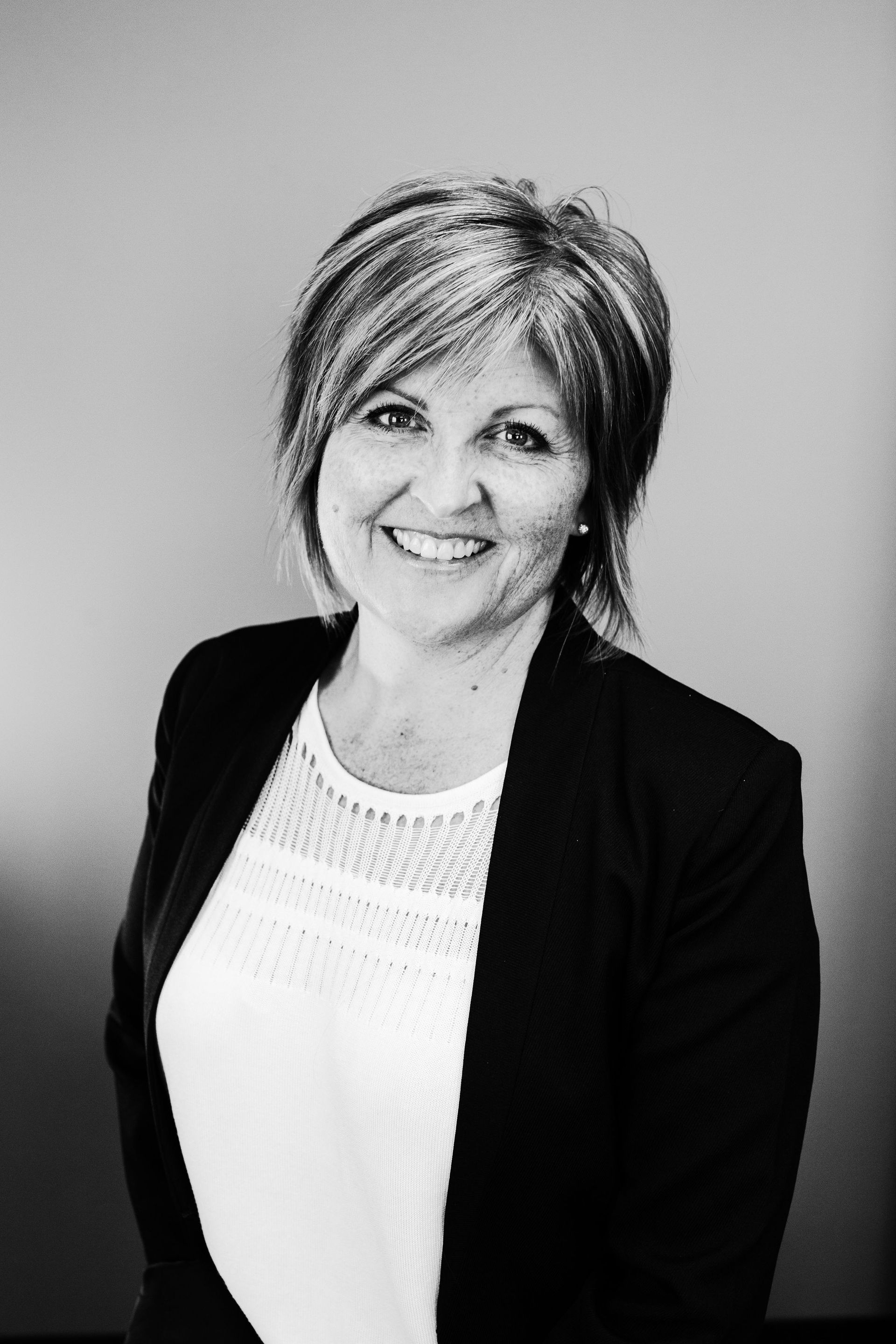 Smiling woman in a black blazer and white top against a plain gray background