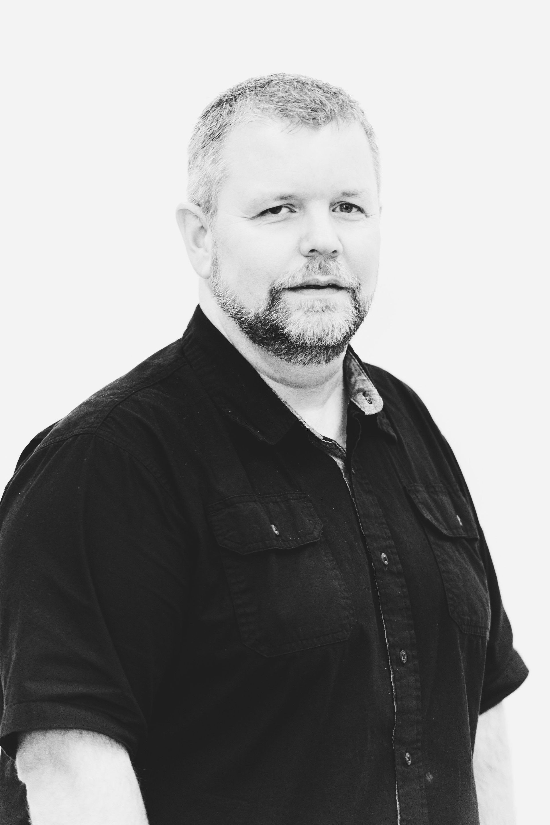 Black-and-white portrait of a bearded man in a dark shirt, facing slightly to the side.