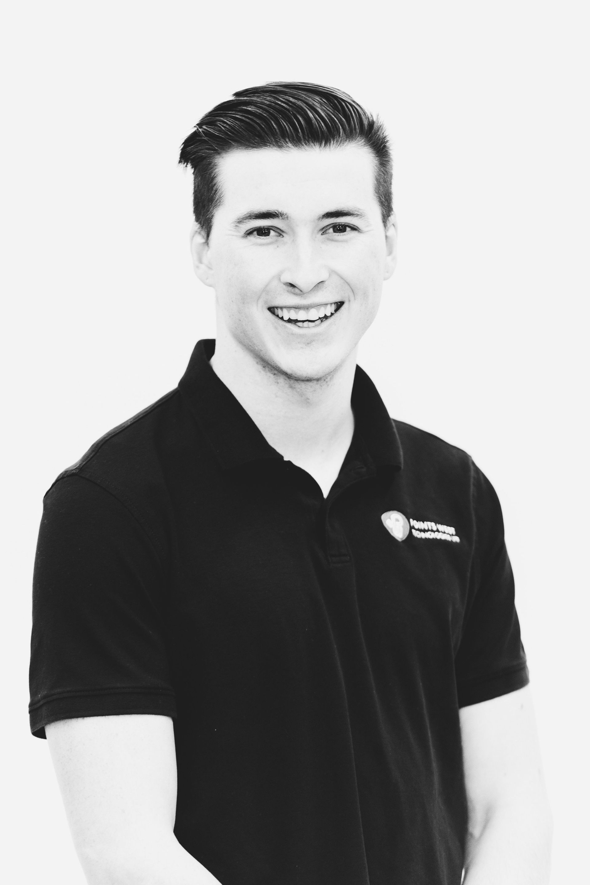 Smiling person in a black polo shirt standing against a light background