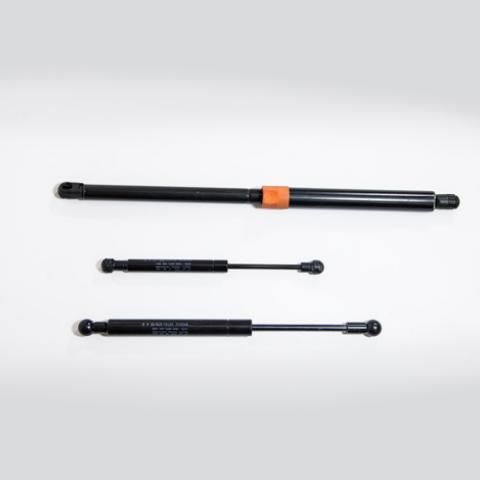 Three black gas struts on a light gray background, one with an orange clip in the center