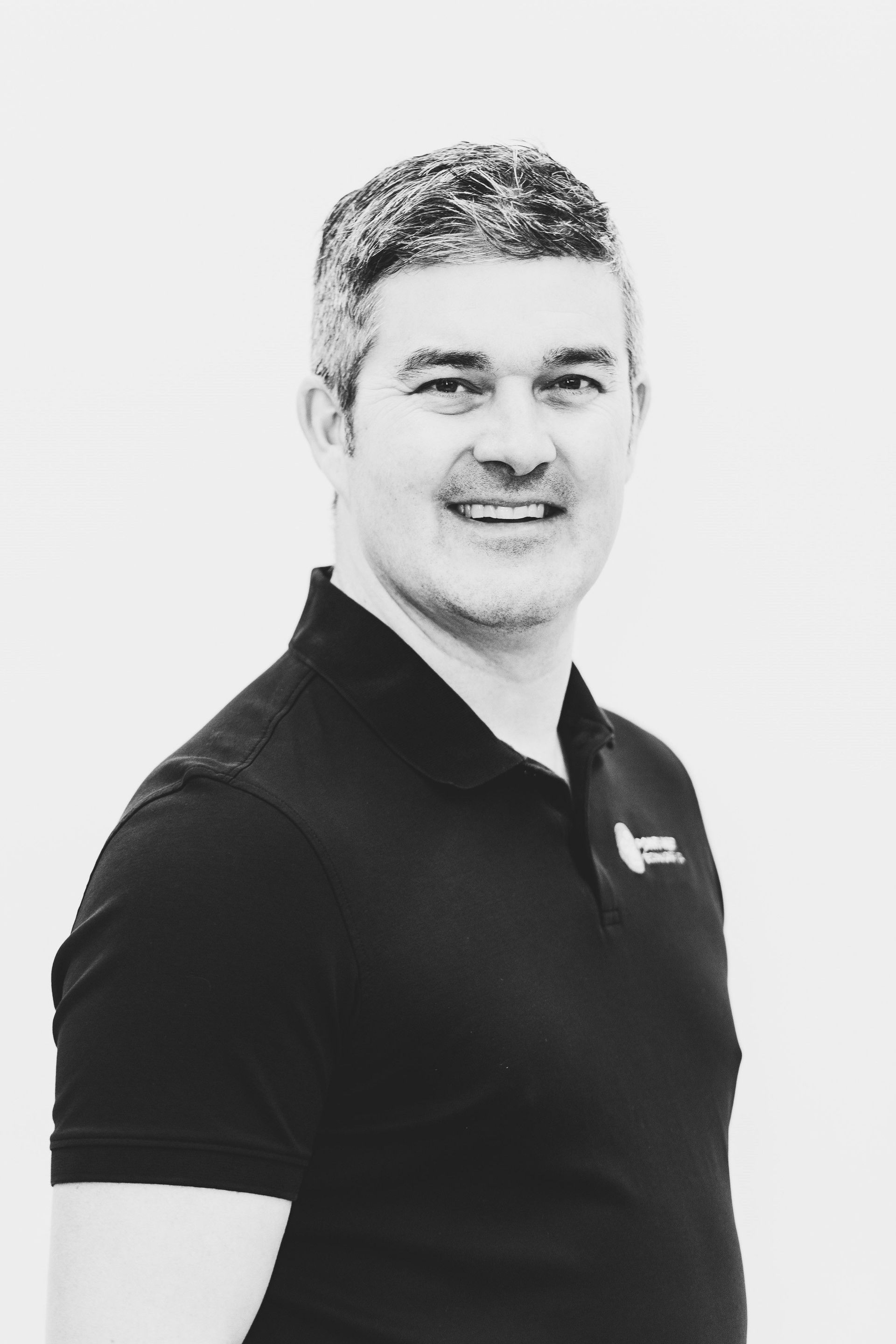 Black-and-white portrait of a smiling man in a dark polo shirt against a plain background