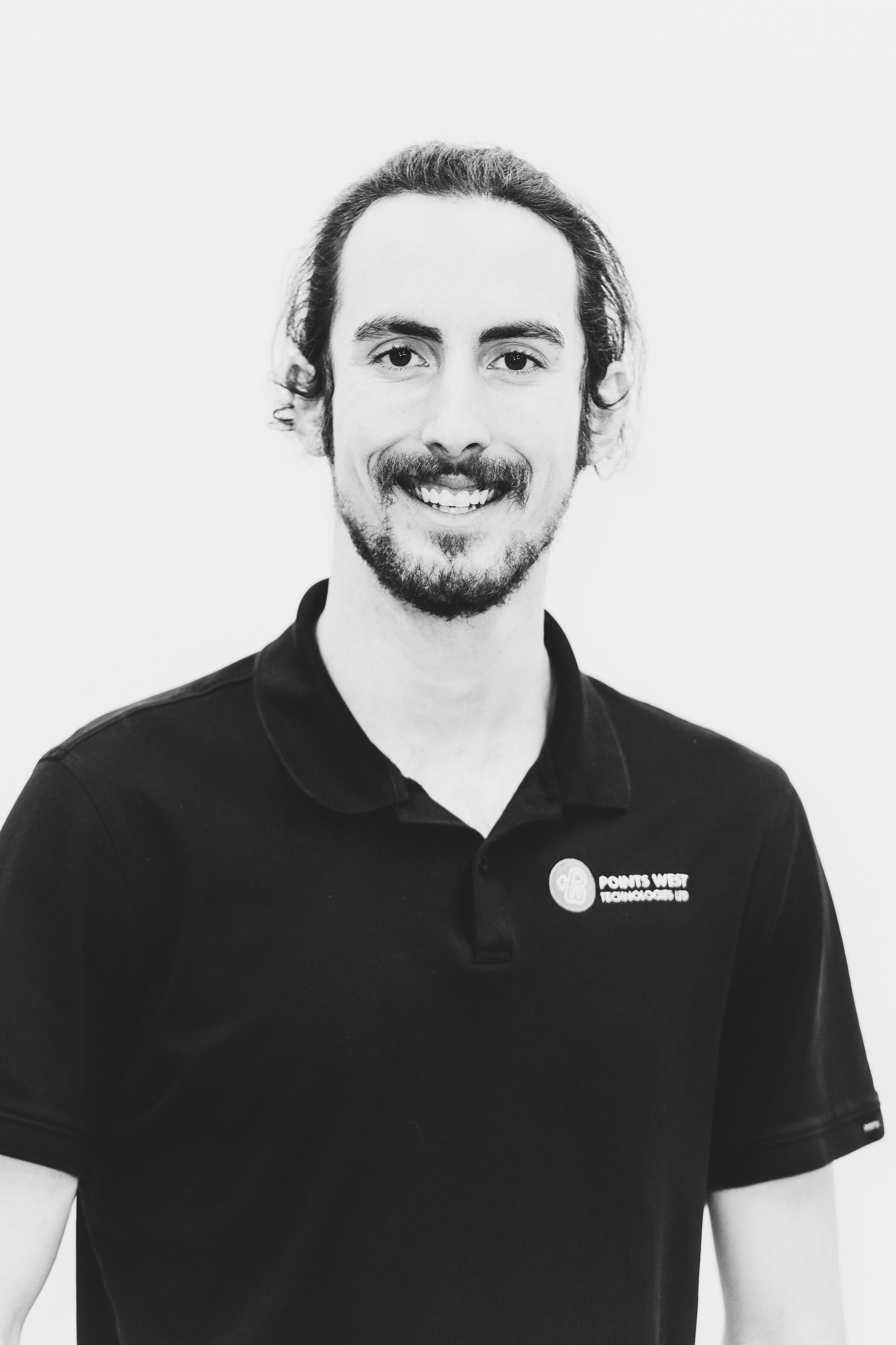 Man in a black polo shirt smiling against a plain light background