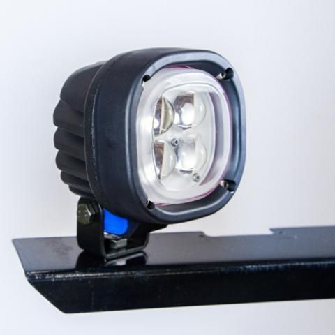 Black LED work light mounted on a bracket against a light background