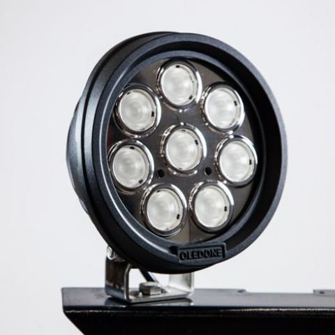 Black round LED spotlight with seven lights mounted on a bracket against a white background