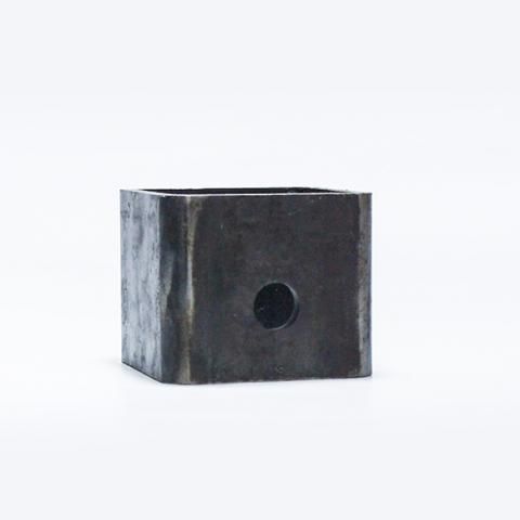 Small dark metal cube with a round hole on one face, isolated on a white background