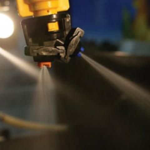 Close-up of a yellow street sweeper spraying water on a road at dusk