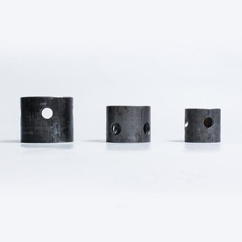 Three small black cylindrical metal parts with holes, arranged on a white background