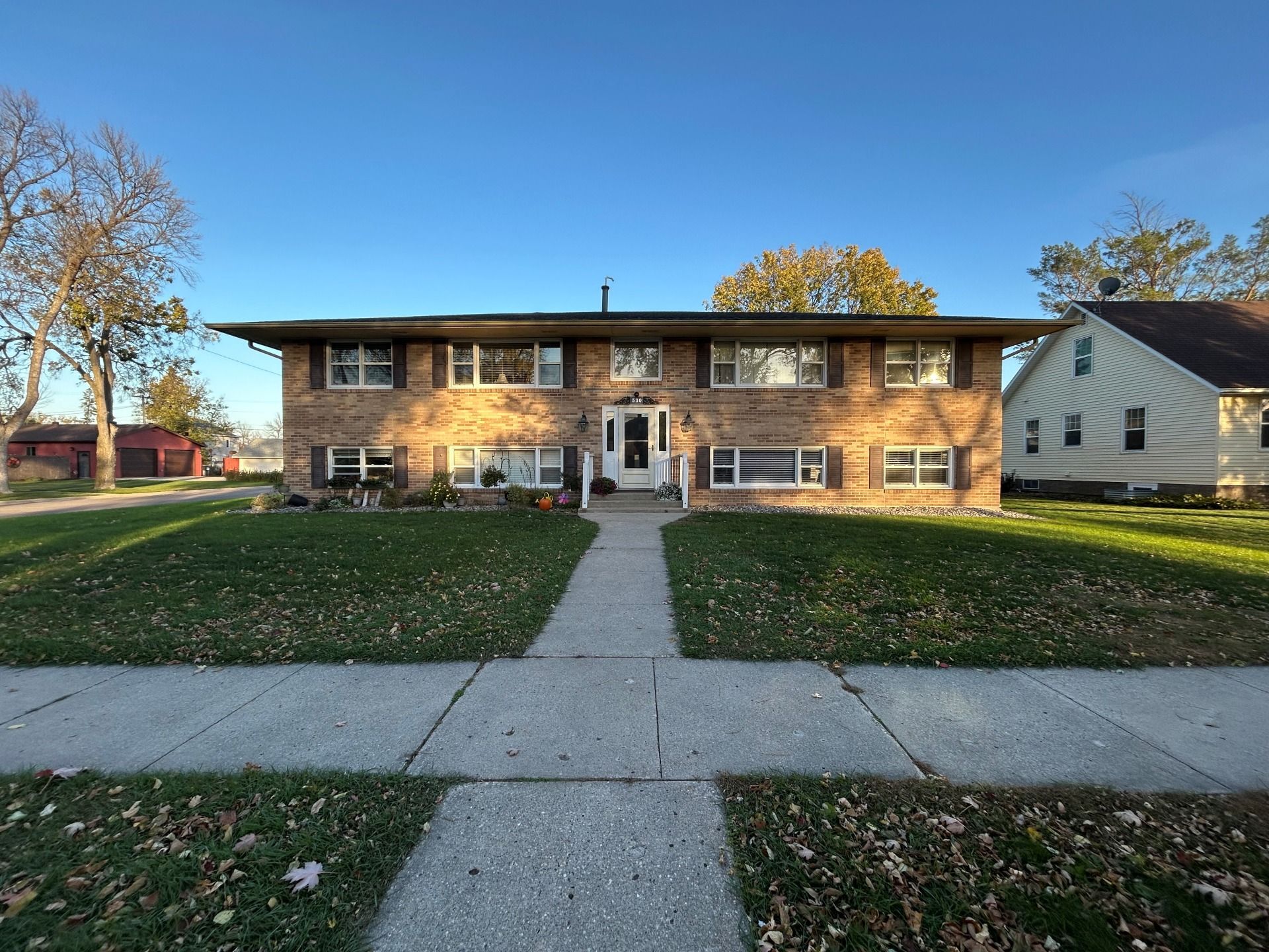 Two-story brick apartment building with a sidewalk, grassy lawn, and clear blue sky.