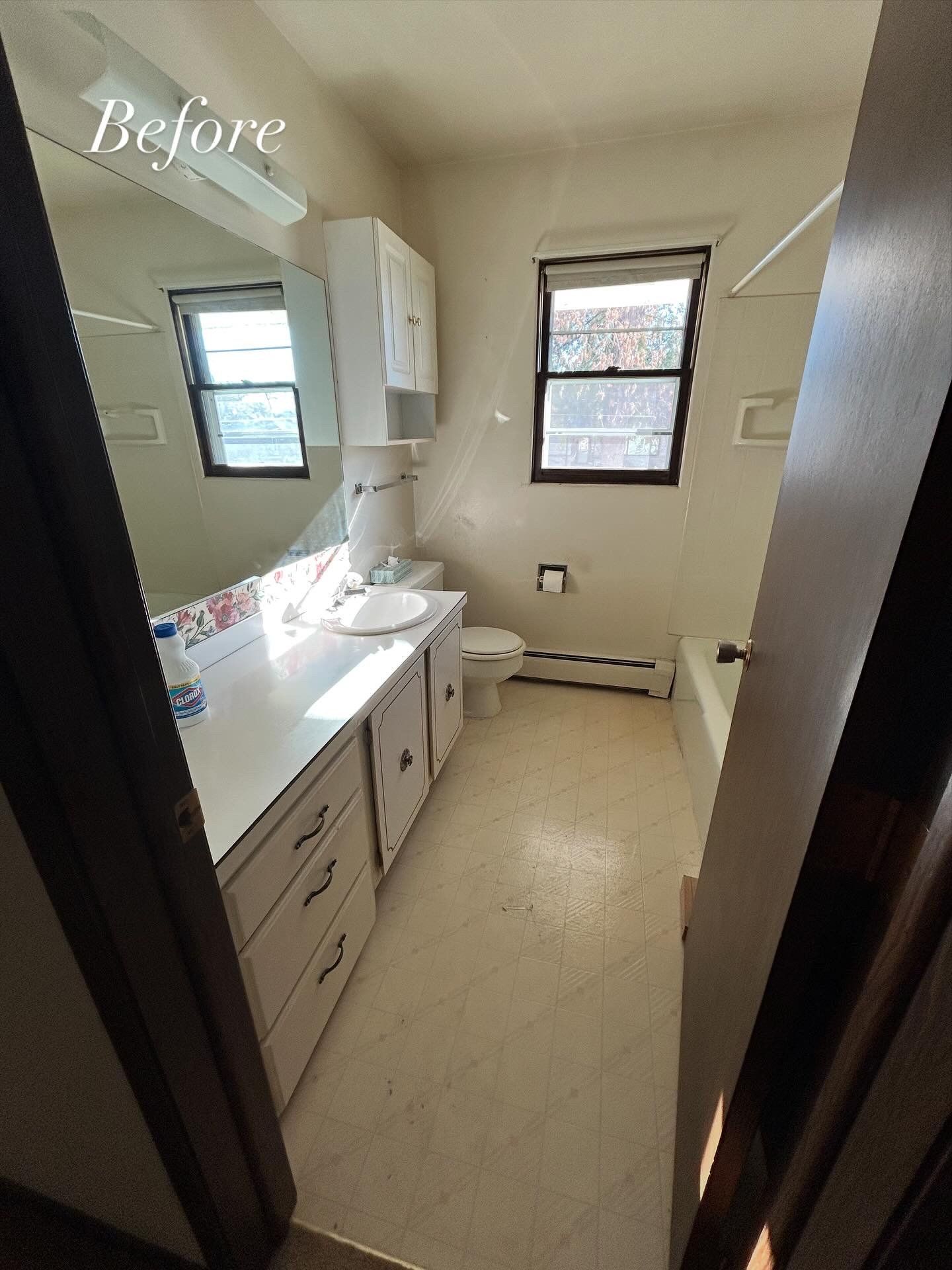 Bathroom with white vanity, toilet, and bathtub; beige walls and floor; small windows.