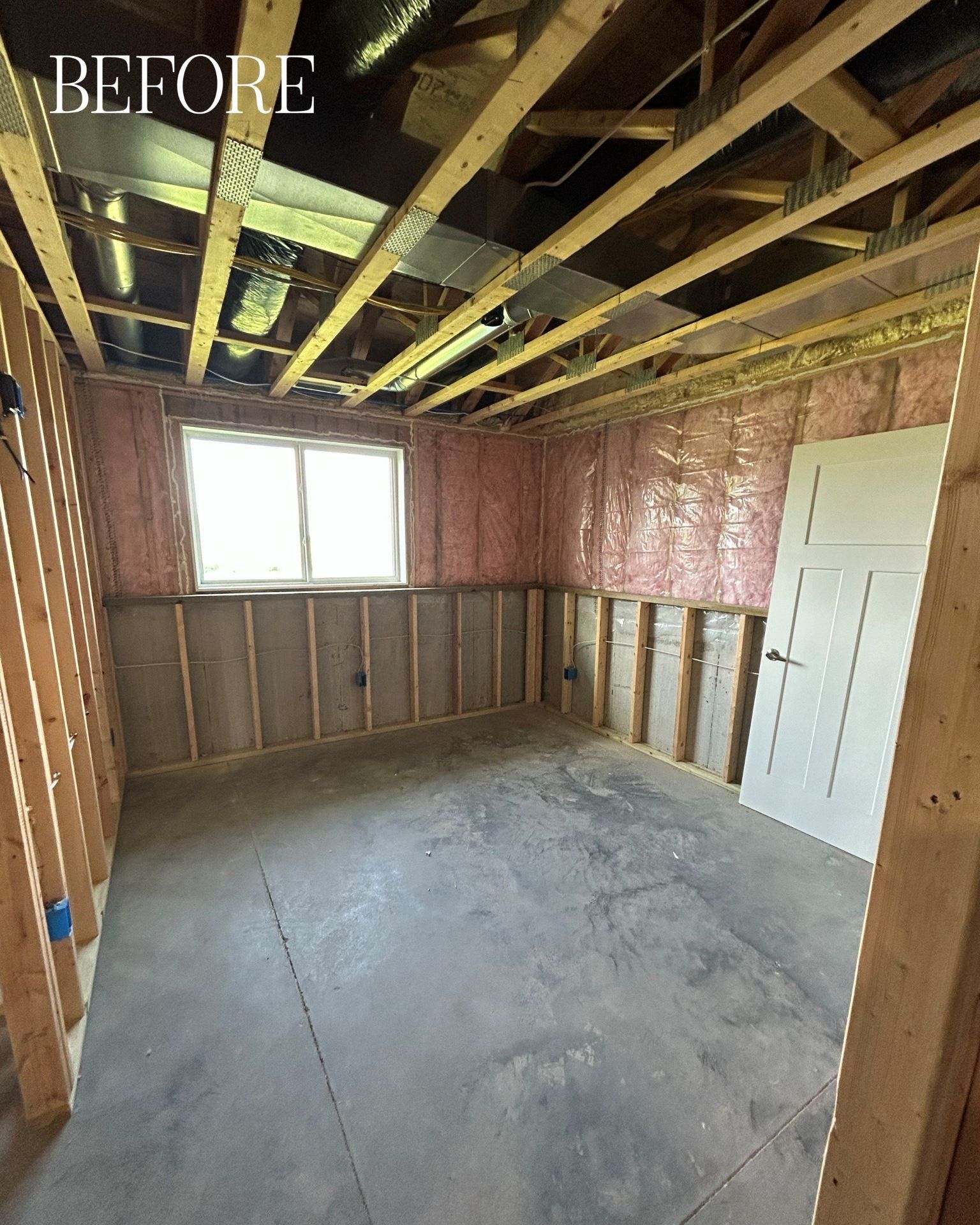 Unfinished basement room with exposed wood framing, insulation, concrete floor, and a window.