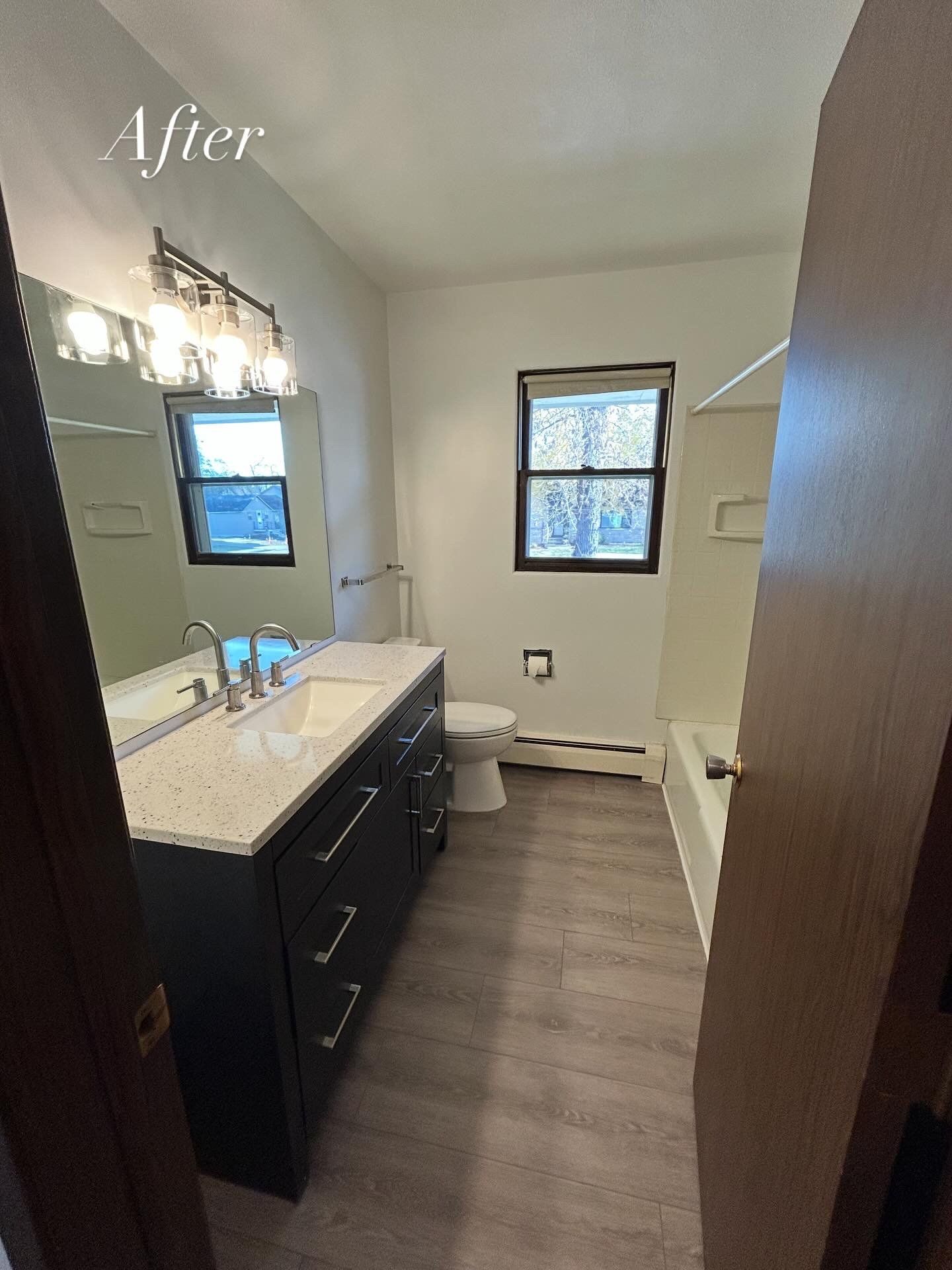 Remodeled bathroom with dark vanity, gray floor, white walls, and a window.