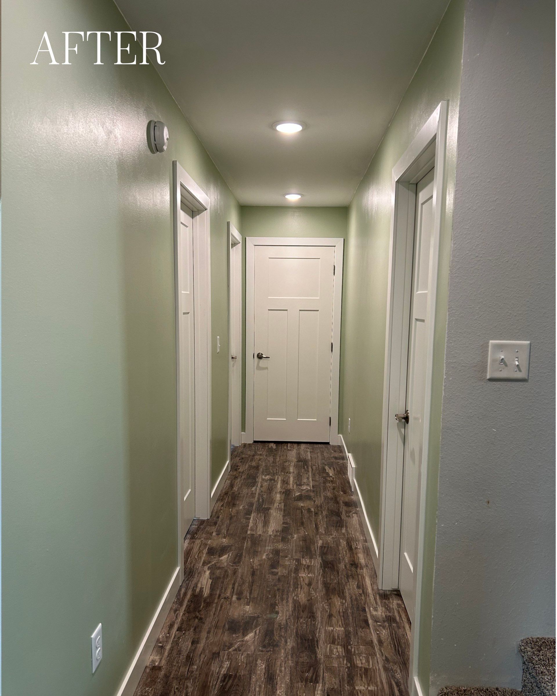 Narrow hallway with pale green walls, white doors, and wood-look flooring.
