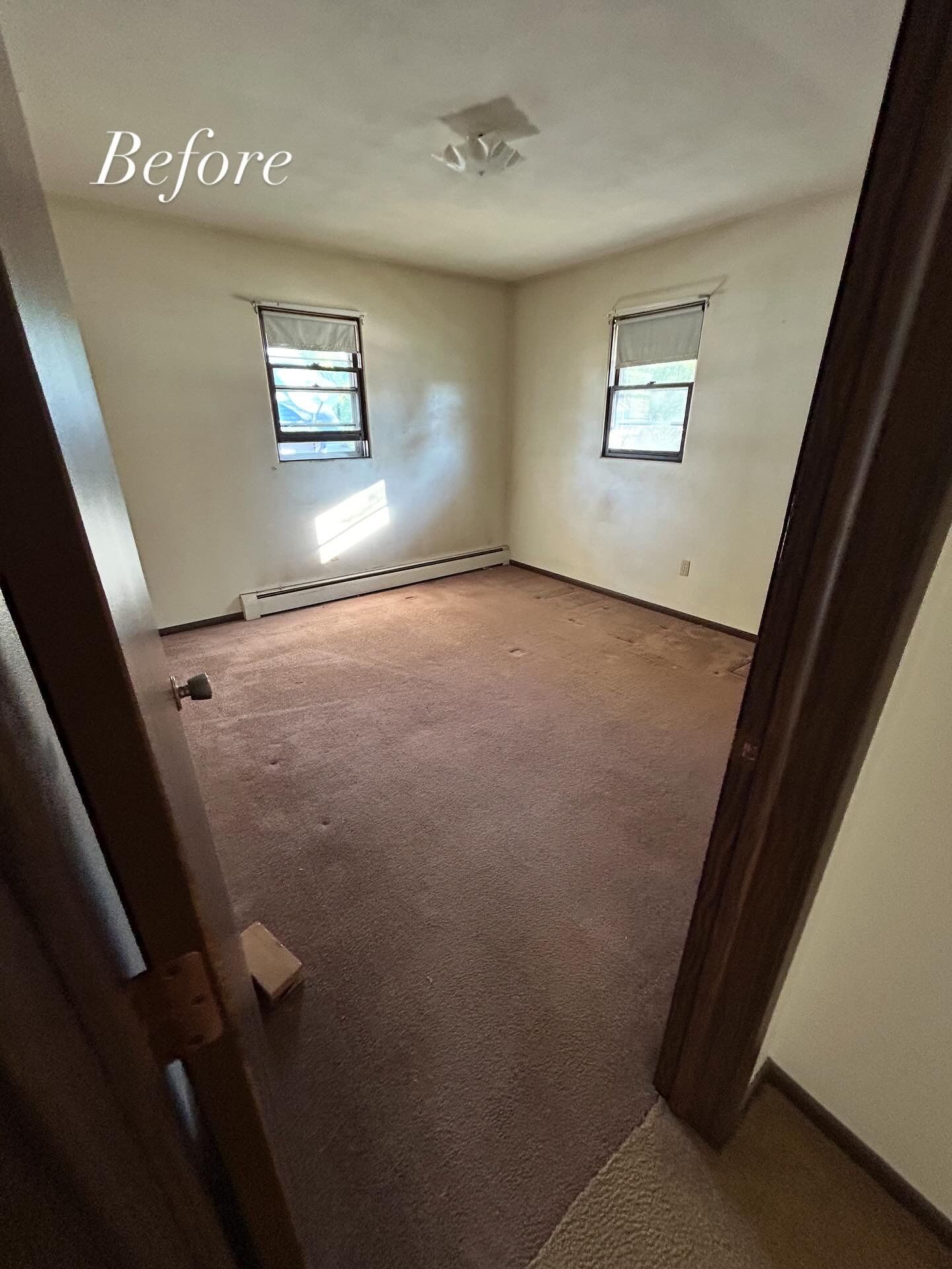 Empty room with brown carpet, two windows, and off-white walls. 