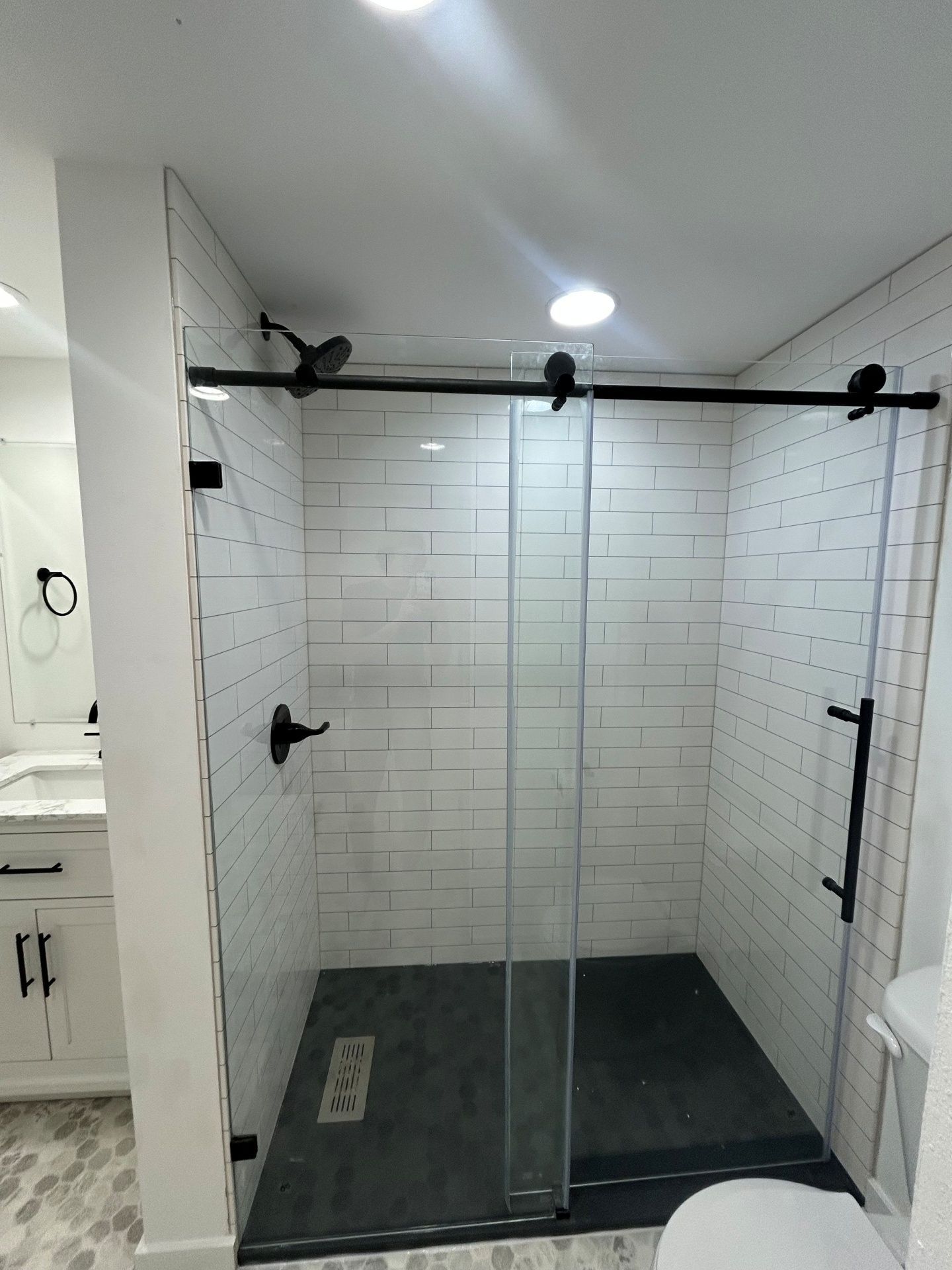 Modern bathroom with a glass shower enclosure and black hardware. White subway tile, dark gray shower floor.