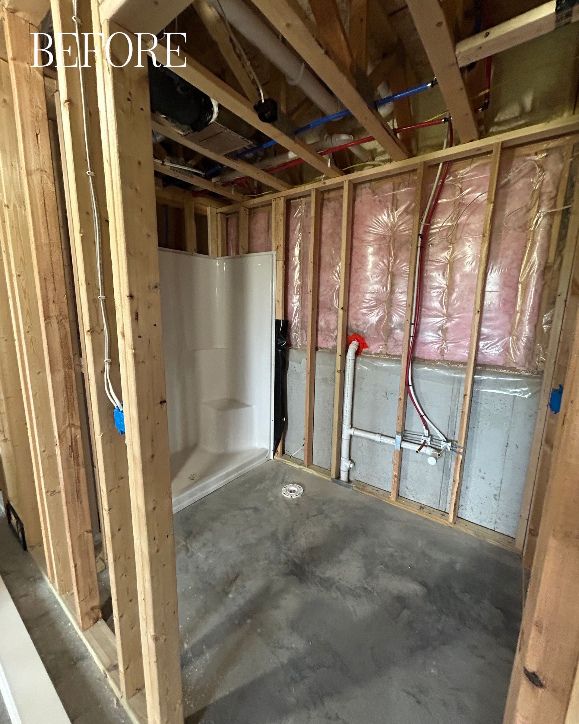 Unfinished bathroom with framed walls, shower stall, insulation, and concrete floor. Plumbing and electrical wiring are exposed.