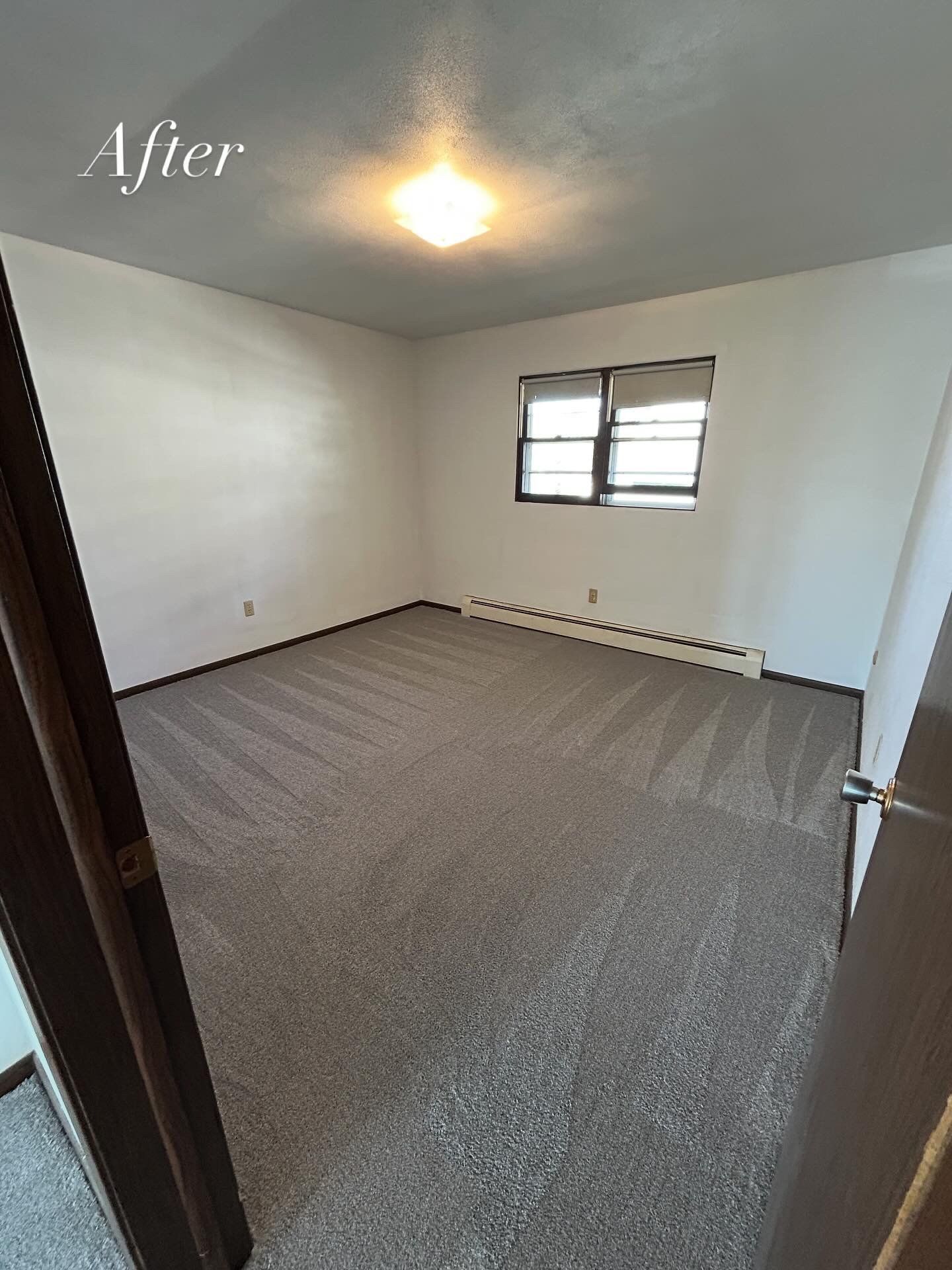 Empty room with new gray carpet, white walls, and a window. 