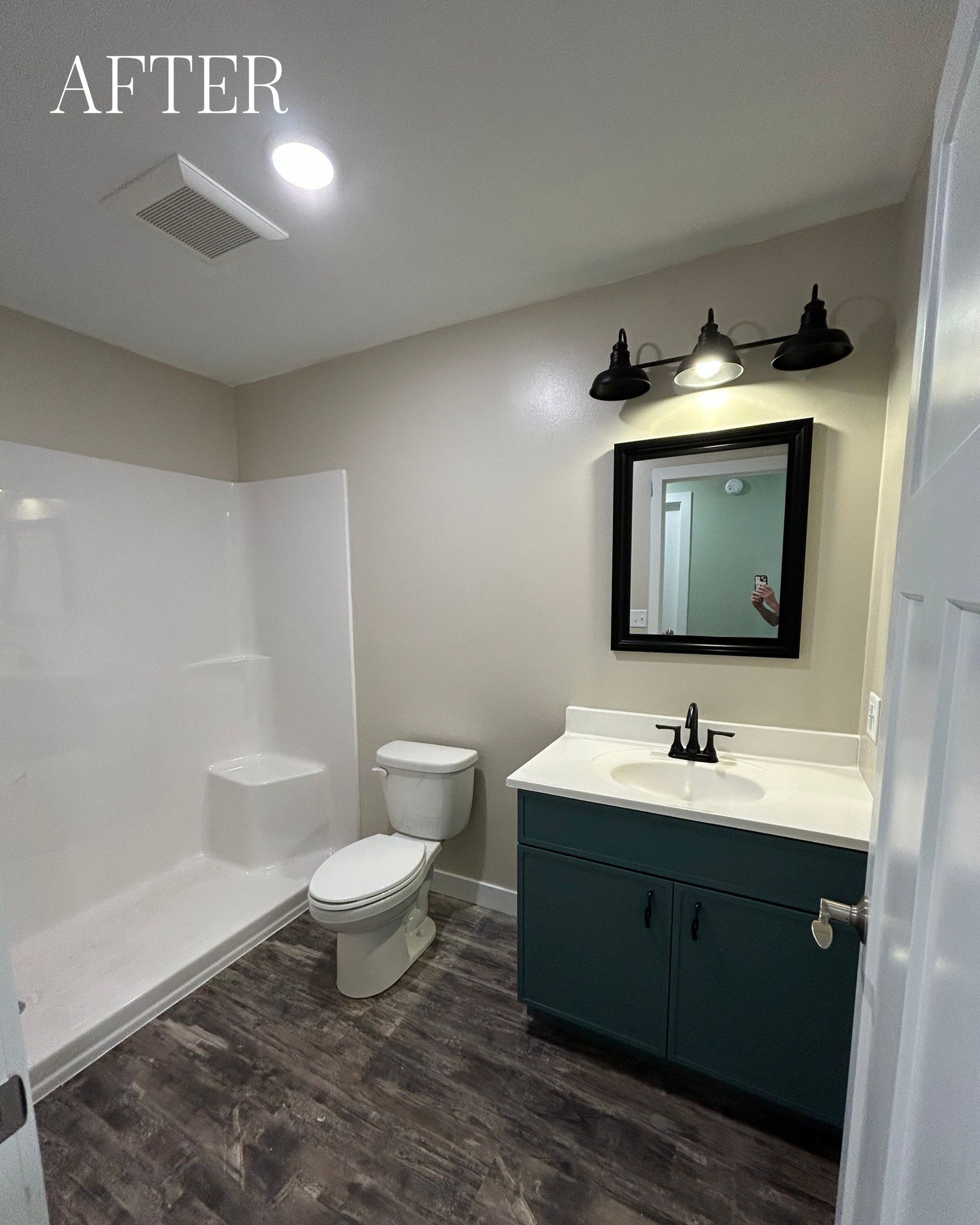 Bathroom with teal vanity, white shower, dark wood-look floor, and black mirror frame.