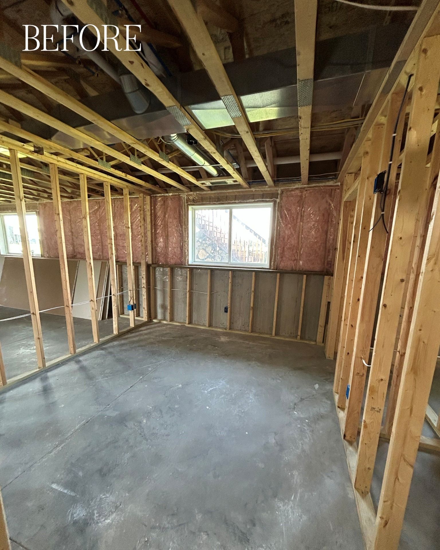 Basement renovation in progress. Wood framing and pink insulation visible. Concrete floor. Window in the back.