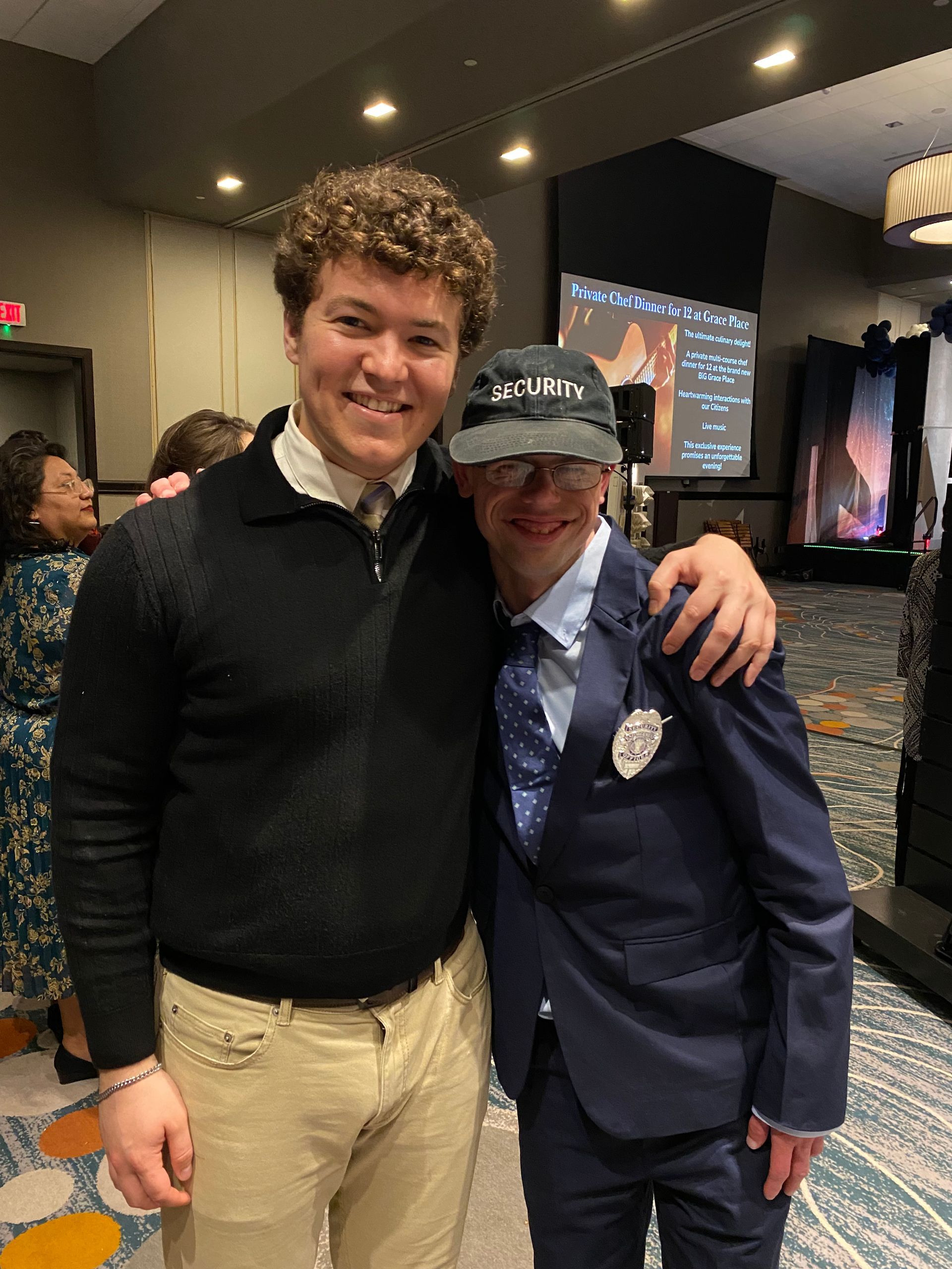 Two men are posing for a picture together in a room . one of the men is wearing a hat.