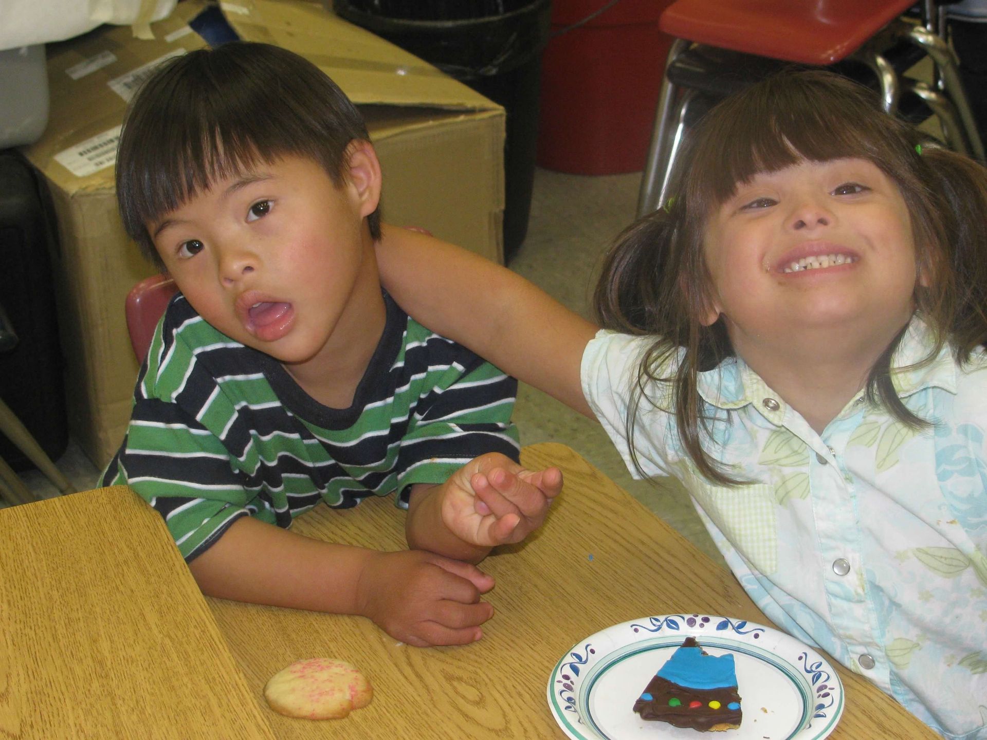 A boy and a girl are sitting at a table with a plate of cookies