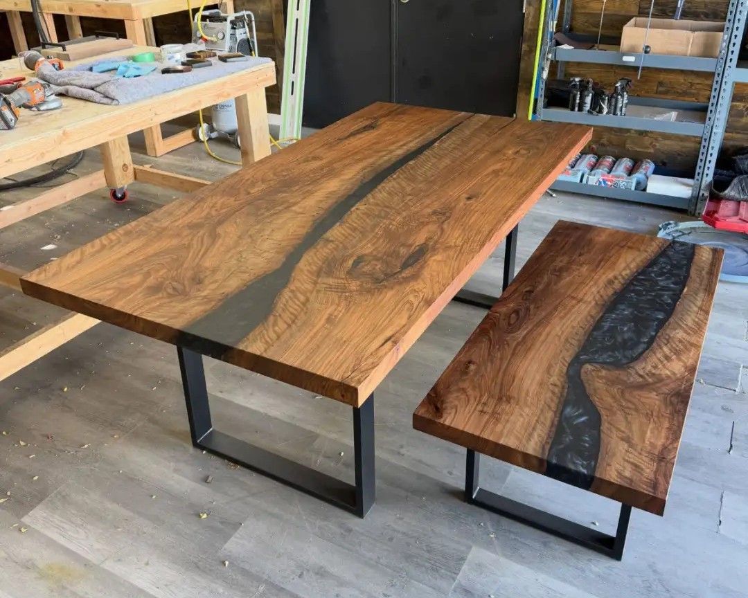 Wood slab dining table and matching bench with black metal legs in a workshop.