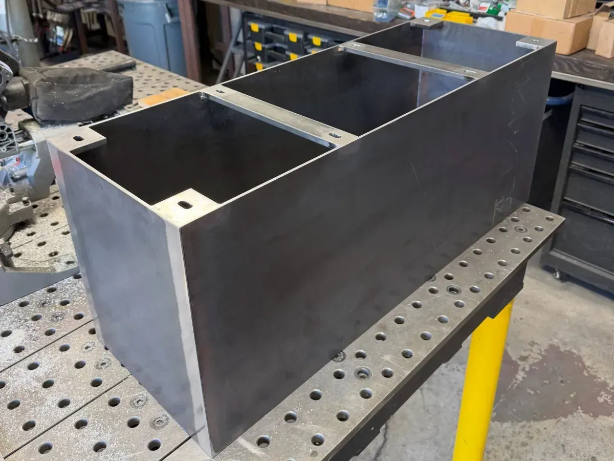 Large black metal rectangular box with two internal compartments on a workshop table