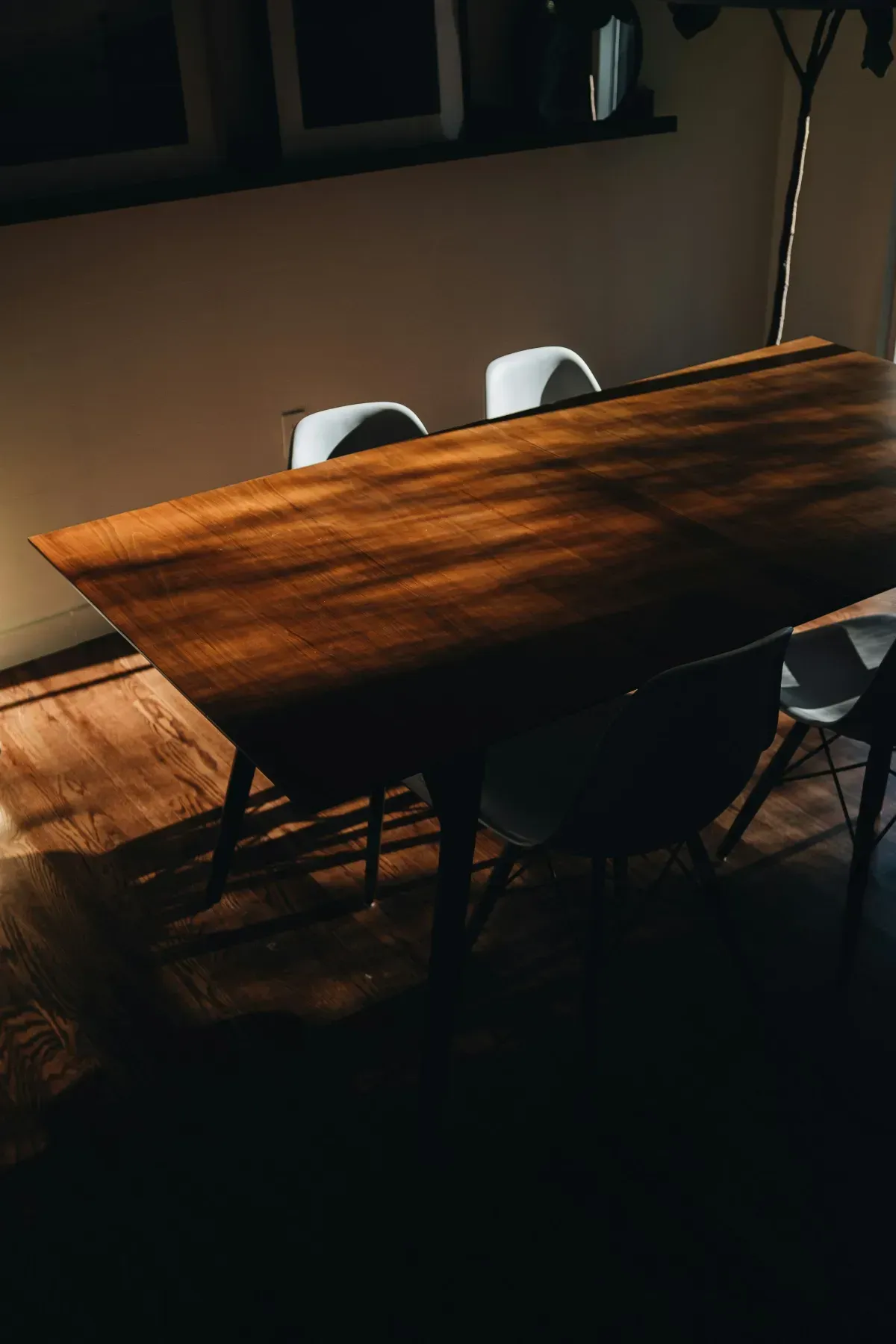Sunlit wooden dining table with white chairs in a dim room