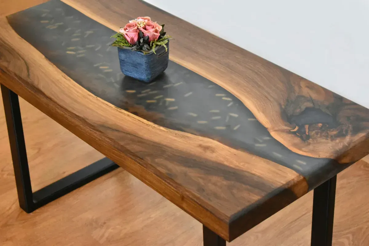Wooden table with black resin center and a small blue vase of pink flowers on top