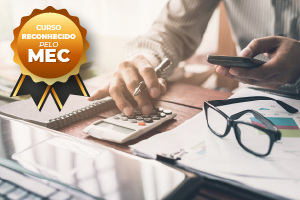 Pessoa usando calculadora e celular, com óculos e papéis sobre a mesa. Curso reconhecido pelo crachá do MEC.
