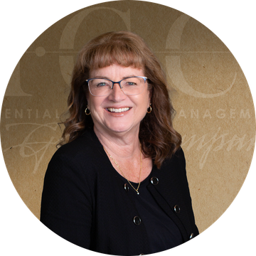 Smiling woman wearing glasses, black jacket, posing for a headshot in front of a neutral background.