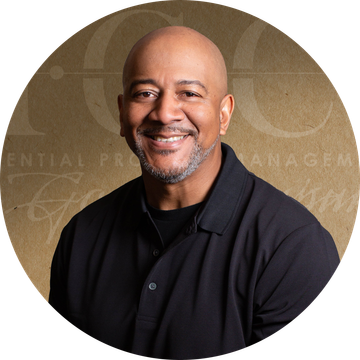 Smiling bald man wearing a black shirt, set against a brown background with text.