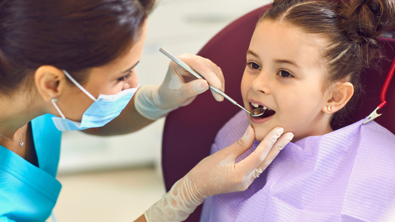 A young boy is sitting in a dental chair giving a thumbs up.