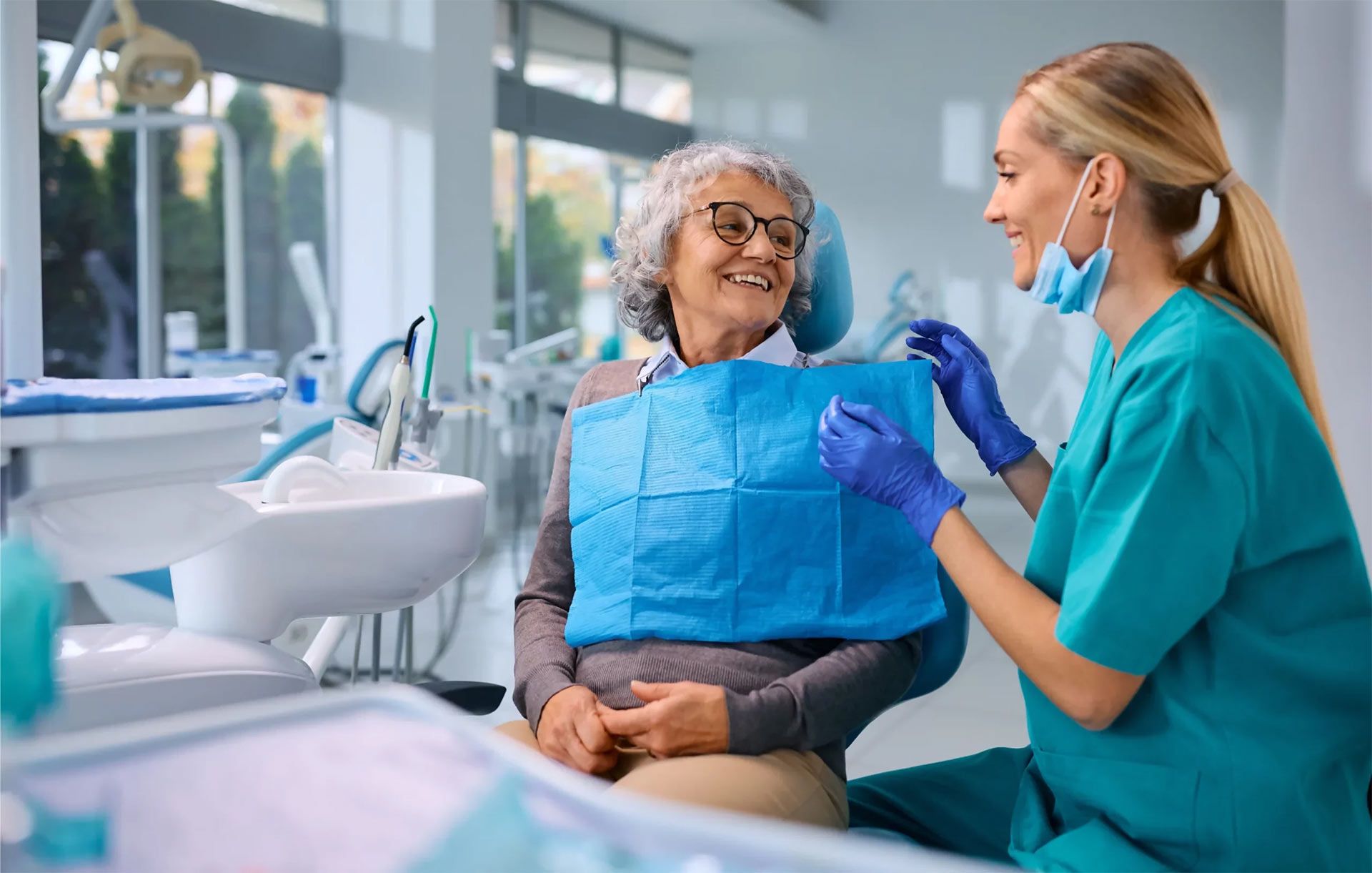 An elderly woman is sitting in a dental chair talking to a dentist.
