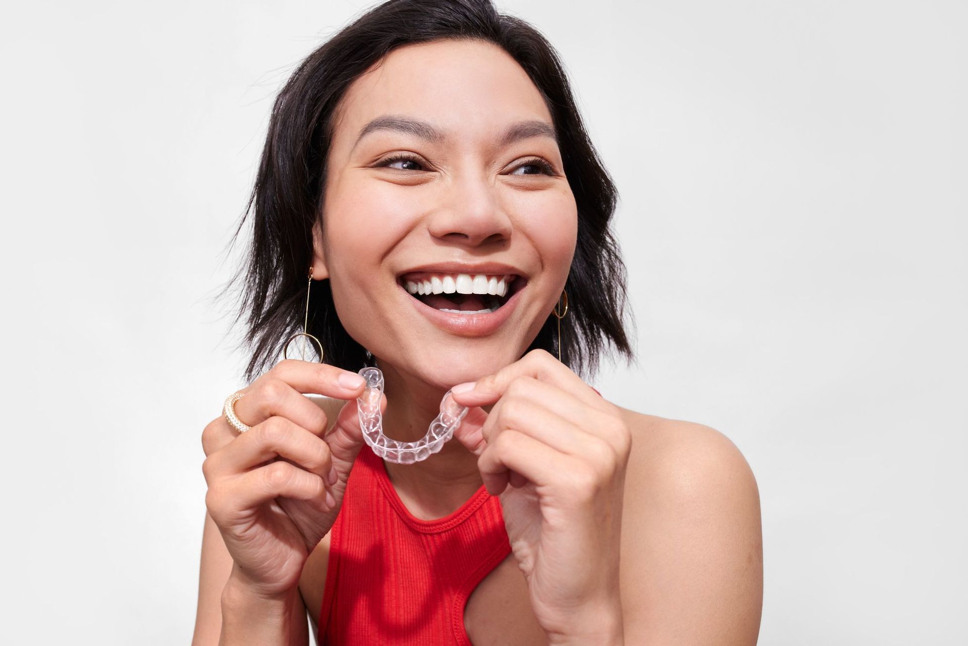 A woman is smiling while holding candidpro clear aligners to her teeth.