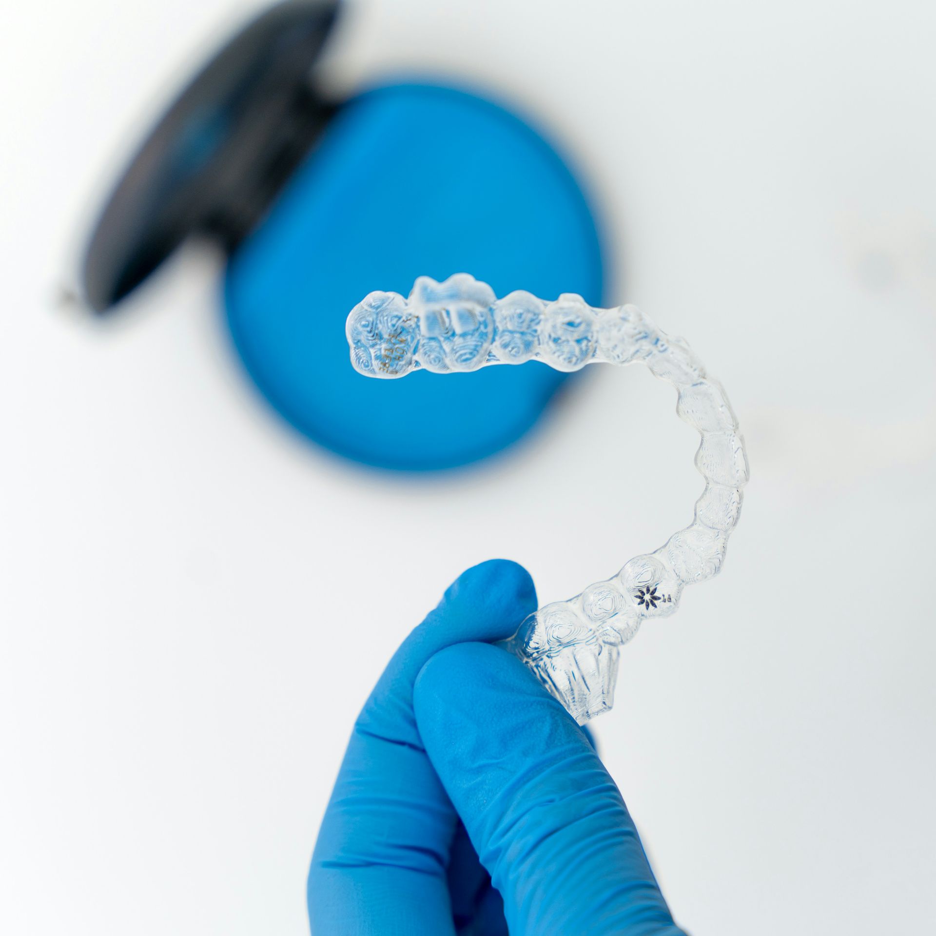 A person wearing blue gloves is holding a clear brace in their hand.