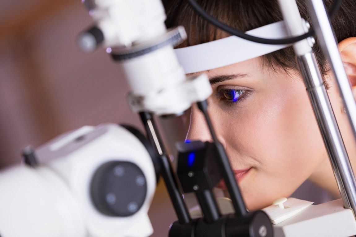 Una persona osserva attraverso un microscopio in laboratorio, con la luce blu che si riflette sull'oculare.