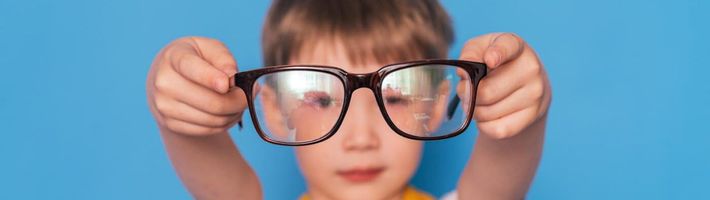 Bambino che tiene in mano grandi occhiali neri su uno sfondo blu brillante