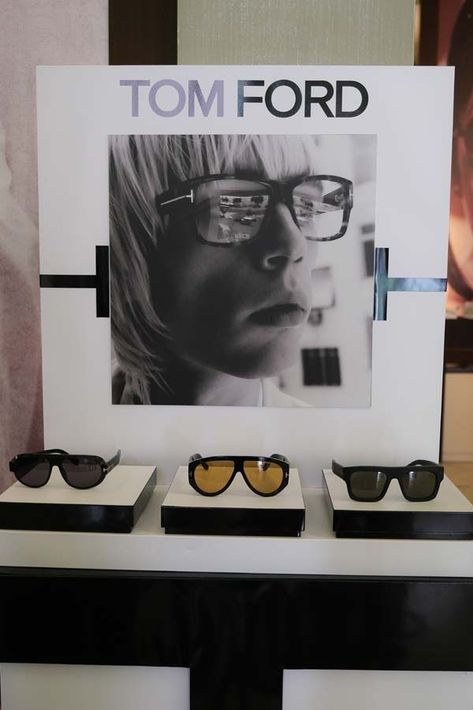 Espositore per occhiali da sole Tom Ford con tre paia su supporti sotto un poster promozionale.