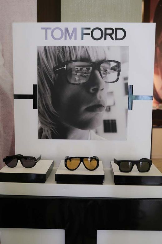 Espositore per occhiali Tom Ford con tre paia di occhiali da sole su un bancone sotto un poster del marchio.