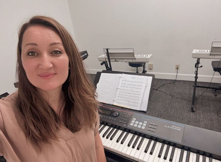 Hands playing a keyboard with sheet music nearby in a warm indoor setting