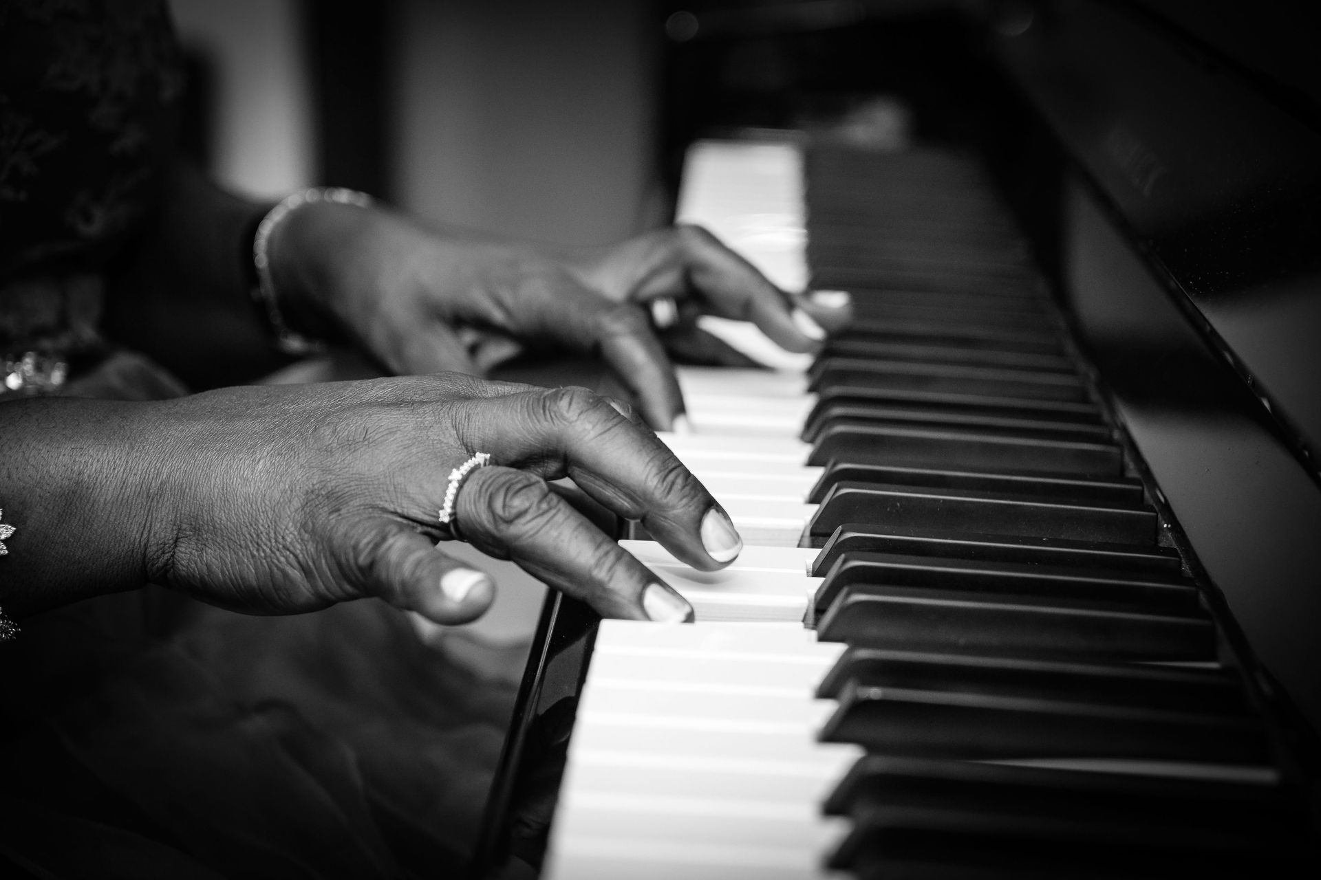 Hands playing a piano keyboard in black and white.