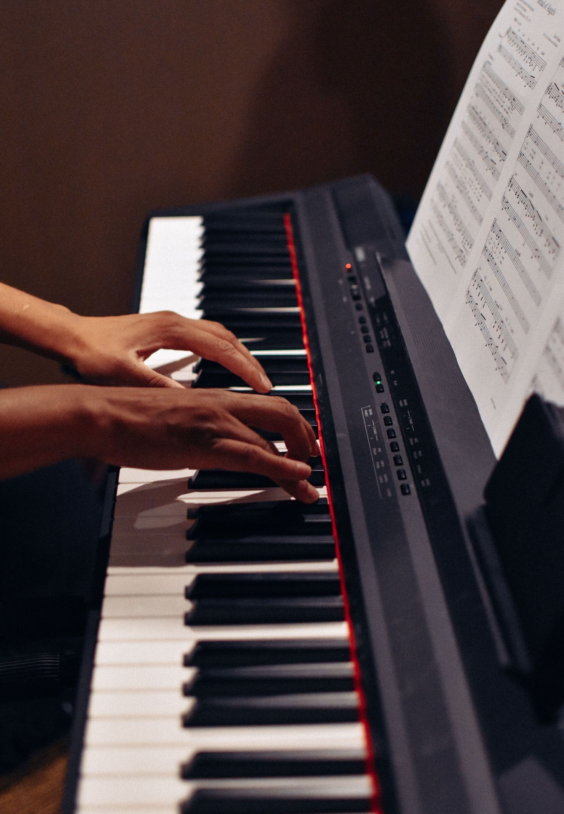 Hands playing a black digital piano with sheet music on the stand
