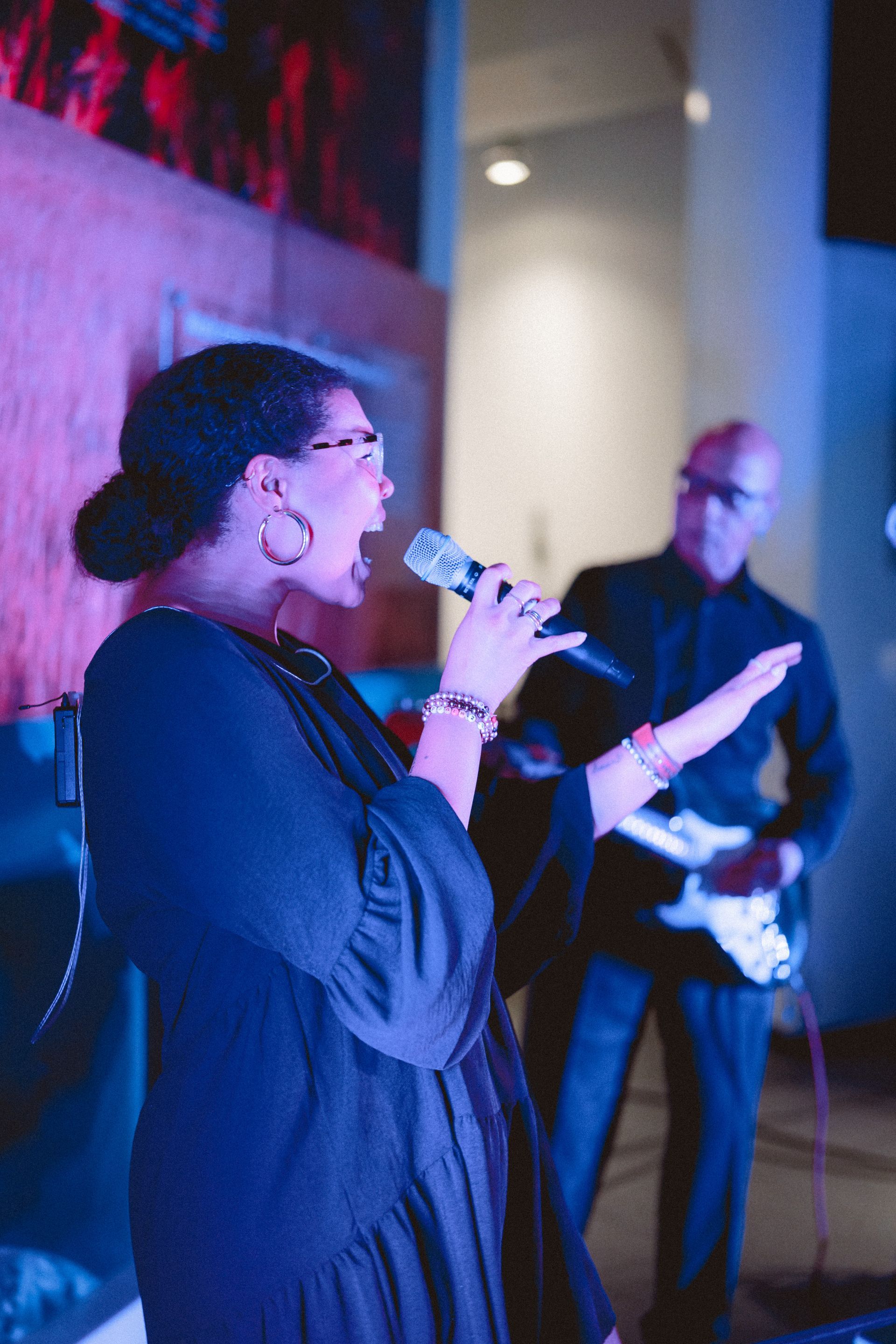 Saxophonist playing on stage with a keyboardist and bassist; buildings in background.