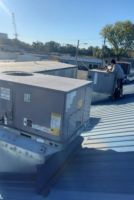 A person works on rooftop HVAC units on a sunny day.