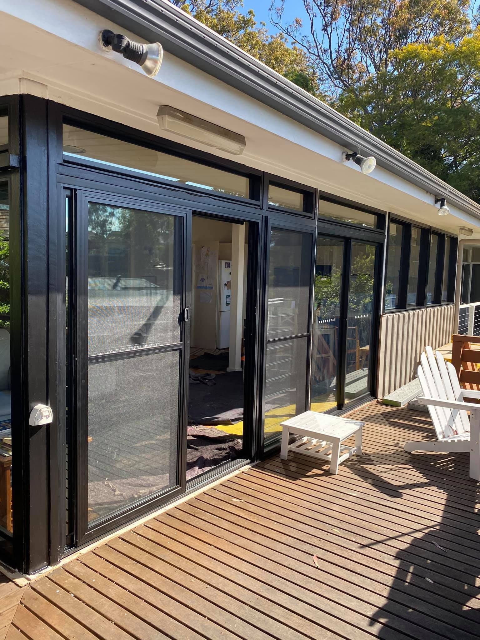 Sliding Glass Doors with Black Frames Open onto A Wooden Deck — Master Glass & Glazing in Maitland, NSW