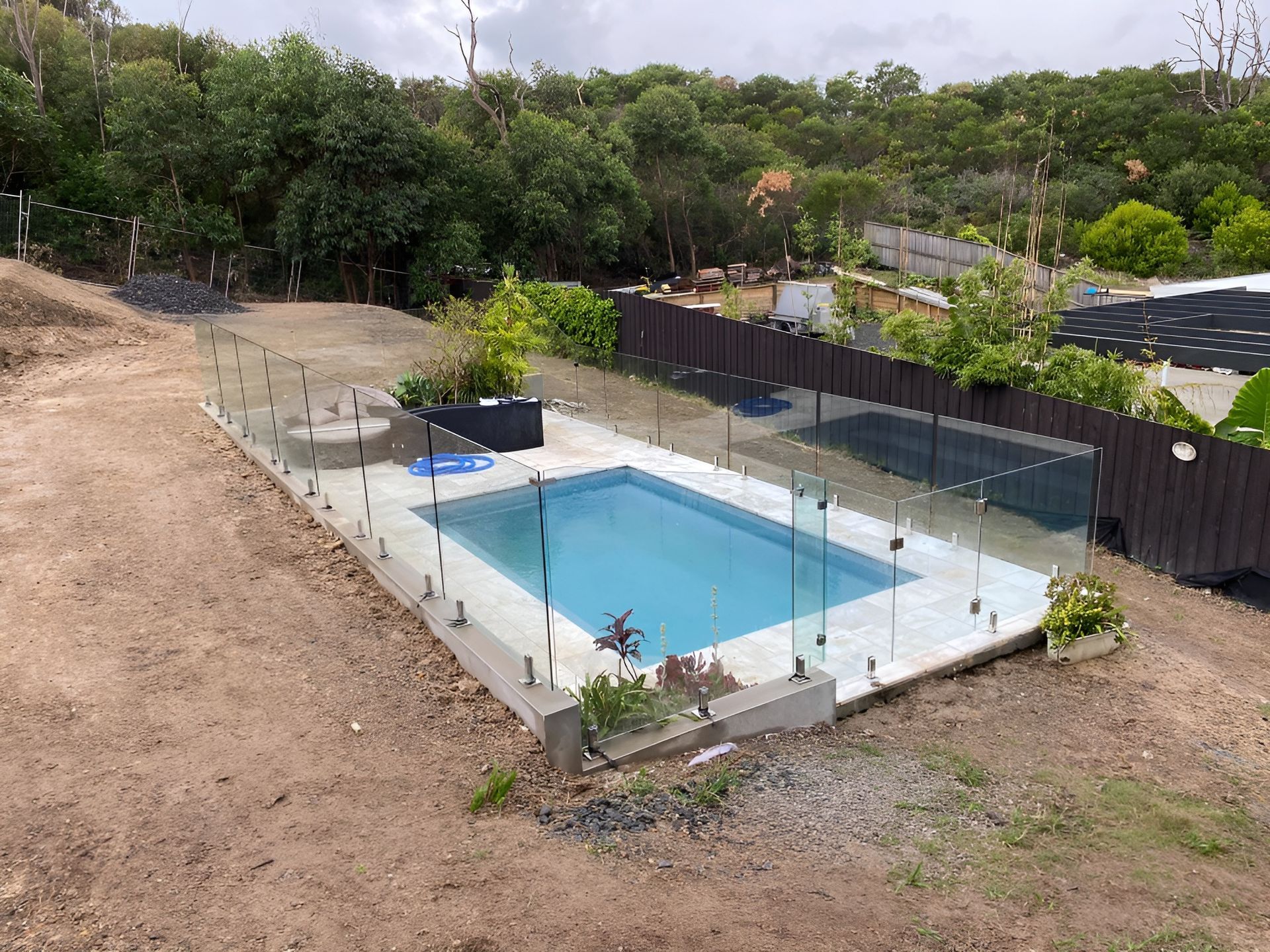 Pool with Glass Fencing in A Backyard, Surrounded by Dirt and Trees — Master Glass & Glazing in Merewether, NSW