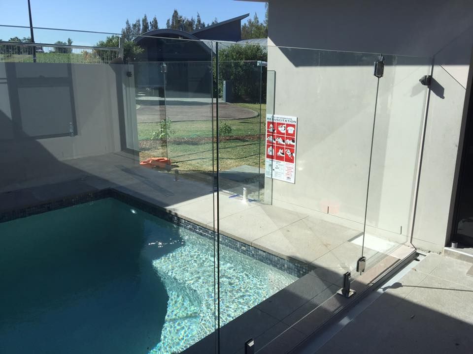Glass Pool Fence Around a Pool, Next to A Building. Safety Sign on The Wall — Master Glass & Glazing in Mayfield, NSW